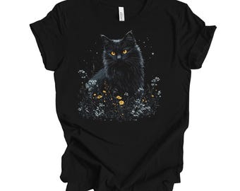 Puede incluir: Camiseta negra con un gato negro sentado en un campo de flores amarillas. El gato tiene ojos amarillos brillantes.