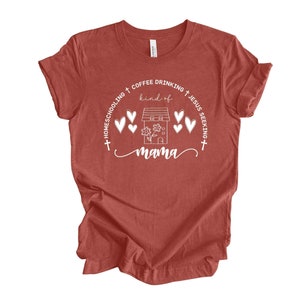 Puede incluir: Una camiseta roja con un dise&ntilde;o gr&aacute;fico blanco que dice "Homeschooling + Coffee Drinking + Jesus Seeking + kind of mama". El gr&aacute;fico tambi&eacute;n incluye una casa con una flor y corazones.