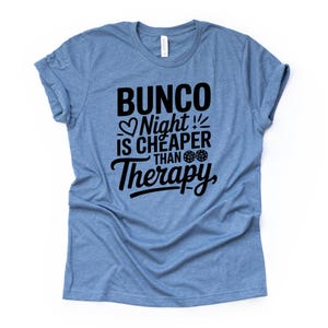 K&ouml;nnte beinhalten: Hellblaues T-Shirt mit dem schwarzen Text "Bunco Night is Cheaper Than Therapy". Der Text enth&auml;lt ein Herz, W&uuml;rfel und einen Blitz. Das T-Shirt ist aus weichem Material.