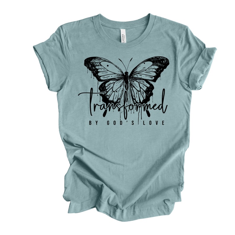 Peut inclure: Un t-shirt bleu clair avec un motif de papillon noir et le texte "transform&eacute; par l'amour de Dieu".