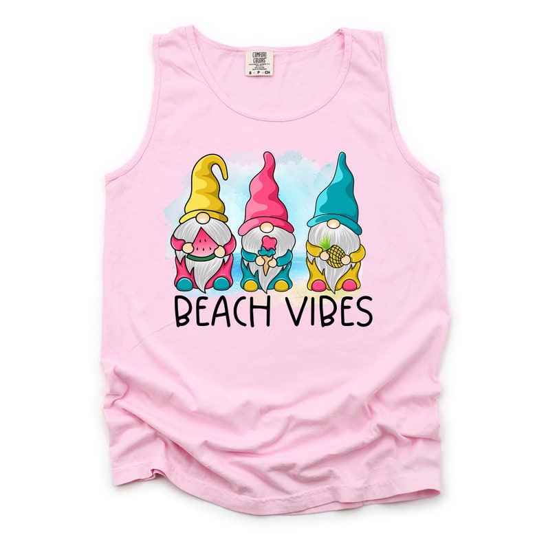 Pu&ograve; includere: Canotta rosa senza maniche con una grafica di tre gnomi che tengono dolcetti estivi. Gli gnomi indossano cappelli colorati e sono in piedi davanti a uno scenario di spiaggia. Il testo "Beach Vibes" &egrave; stampato sotto gli gnomi.