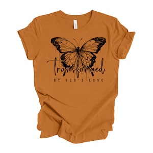 Peut inclure: Un t-shirt jaune moutarde avec un motif de papillon noir et le texte "Transform&eacute; par l'amour de Dieu".