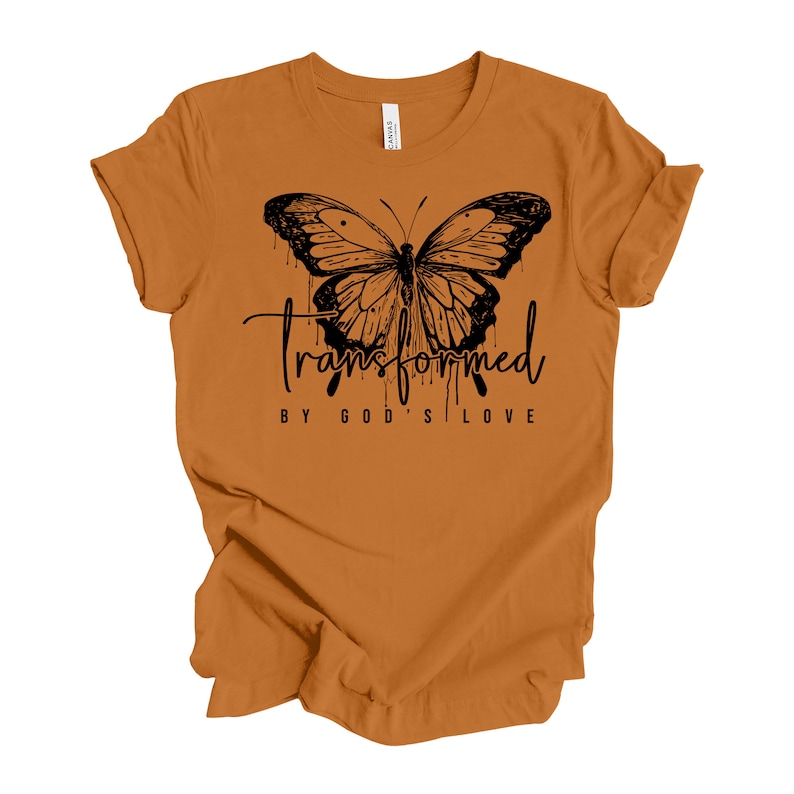 Peut inclure: Un t-shirt jaune moutarde avec un motif de papillon noir et le texte "Transform&eacute; par l'amour de Dieu".