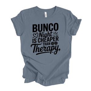 K&ouml;nnte beinhalten: Ein blaues T-Shirt mit dem schwarzen Text "Bunco Night is Cheaper Than Therapy". Das Design beinhaltet ein Herz, W&uuml;rfel und einen Blitz. Das T-Shirt ist aus weichem Material.