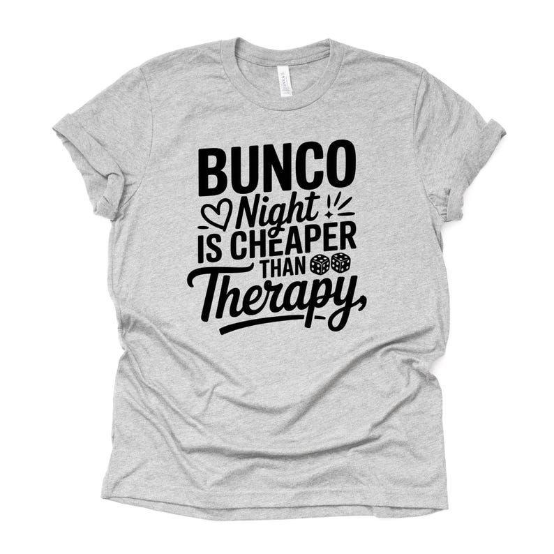 K&ouml;nnte beinhalten: Ein meliertes graues T-Shirt mit dem schwarzen Text "Bunco Night is Cheaper Than Therapy". Das Design umfasst ein Herz, W&uuml;rfel und Ausrufezeichen. Das T-Shirt ist aus weichem Material und hat kurze &Auml;rmel.