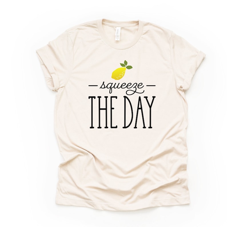 May include: A beige t-shirt with a yellow lemon graphic and the text "squeeze the day" in black.