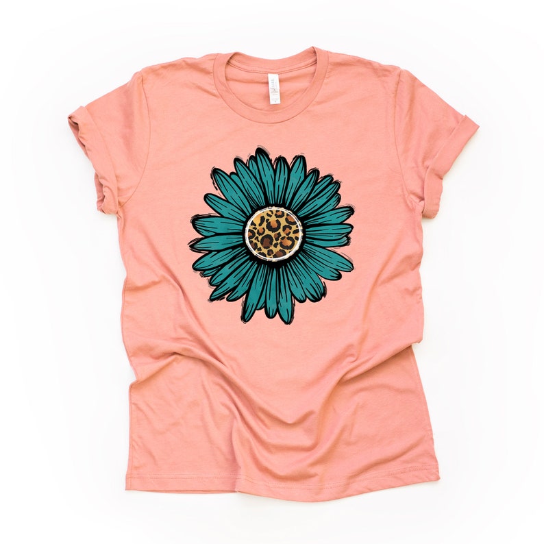 K&ouml;nnte beinhalten: Ein pfirsichfarbenes T-Shirt mit einer blaugr&uuml;nen  Margerite mit einem Leopardenmuster in der Mitte.