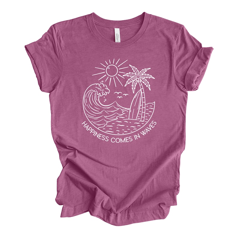 May include: A mauve t-shirt with a white graphic of a wave, palm tree, and sun. The text "Happiness comes in waves" is printed below the graphic.