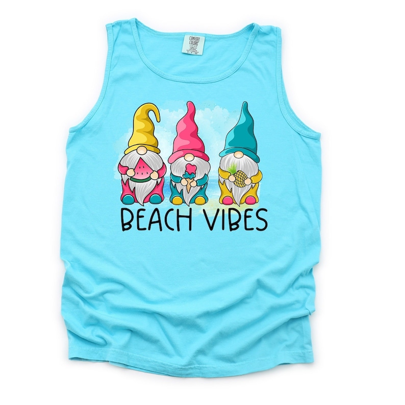 Pu&ograve; includere: Una canotta turchese con una grafica di tre gnomi che tengono dolcetti estivi. Gli gnomi indossano cappelli colorati e tengono una anguria, un cono gelato e un ananas. Il testo "Beach Vibes" &egrave; stampato sotto gli gnomi.