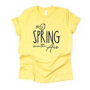 May include: Yellow t-shirt with a black graphic of a bird and the text "SPRING is in the Air".