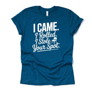 May include: A teal t-shirt with white text that reads "I CAME. I Rolled. I Stole Your Spot." The text is in a mix of fonts, with a small chair graphic. The shirt is made of a soft material.