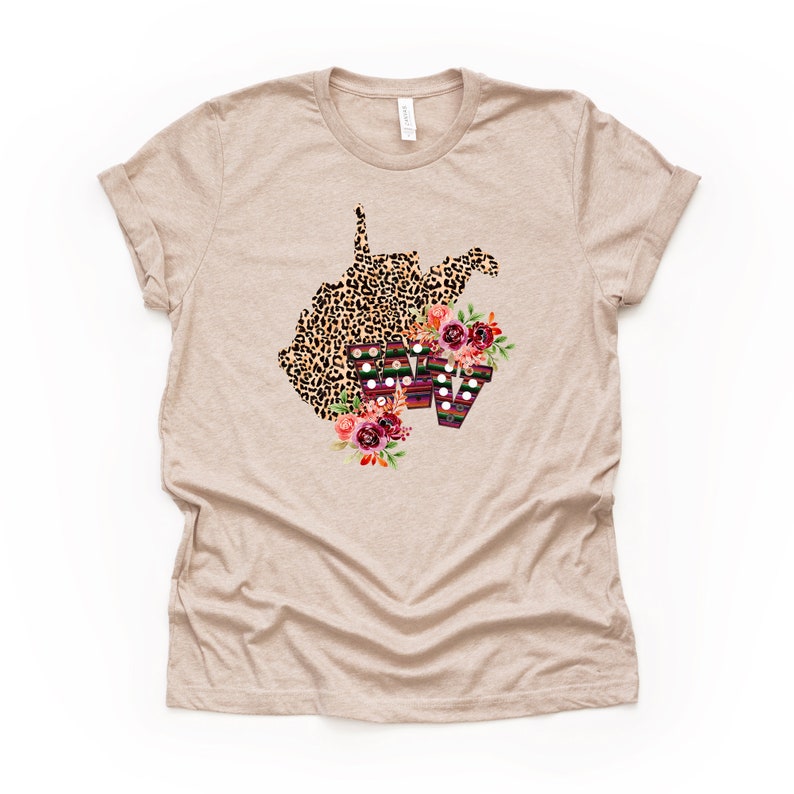 May include: A beige t-shirt with a leopard print outline of the state of West Virginia with floral accents and the letters "WV" in a colorful striped pattern.