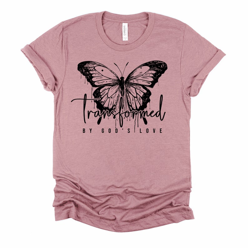 Peut inclure: Un t-shirt mauve avec un motif de papillon noir et le texte "transform&eacute; par l'amour de Dieu".
