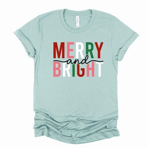 May include: A light blue t-shirt with the text "Merry and Bright" in red, green, white, and pink letters.