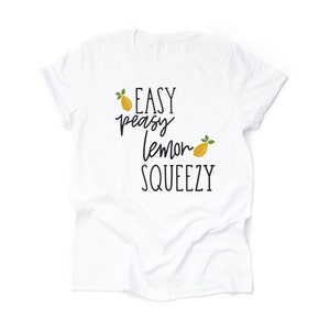 Puede incluir: Camiseta blanca con el texto "Easy peasy lemon squeezy" en letras negras y dos limones amarillos con hojas verdes.