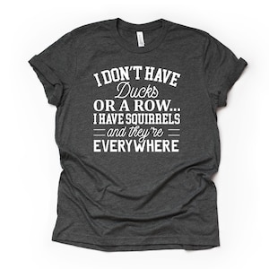 Peut inclure: Un t-shirt gris fonc&eacute; chin&eacute; avec du texte blanc qui dit "Je n'ai pas de canards ou une rang&eacute;e... J'ai des &eacute;cureuils - et ils sont partout".