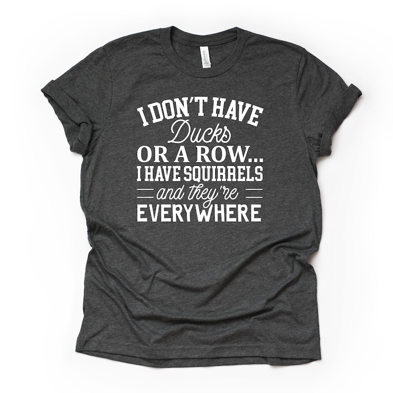 Peut inclure: Un t-shirt gris fonc&eacute; chin&eacute; avec du texte blanc qui dit "Je n'ai pas de canards ou une rang&eacute;e... J'ai des &eacute;cureuils - et ils sont partout".