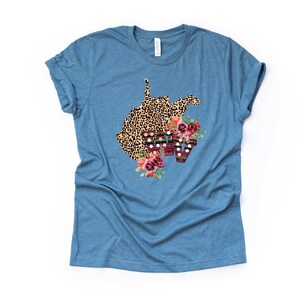 May include: A blue t-shirt with a leopard print outline of the state of West Virginia with floral accents and the letters WV in a colorful patterned font.