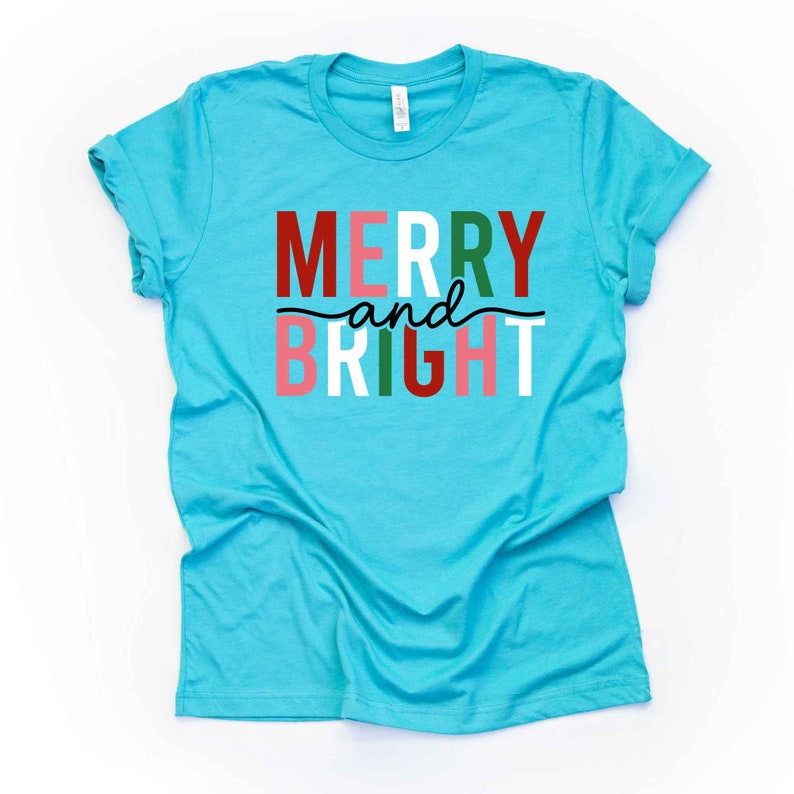 May include: A turquoise blue t-shirt with the text "Merry and Bright" in red, white, green, and pink letters.