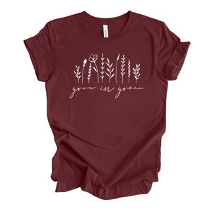 May include: A maroon t-shirt with a white graphic of stylized flowers and the text "grow in grace".