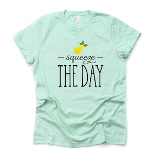 May include: A light green t-shirt with a yellow lemon and the text "squeeze the day" in black.