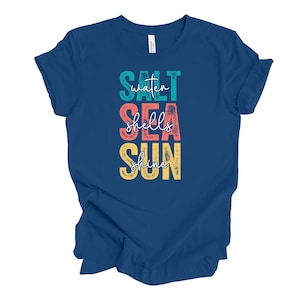 May include: A navy blue t-shirt with the words "Salt Sea Shells Shine" in teal, red, orange, and yellow block letters. The shirt is made of a soft material and is suitable for casual wear.