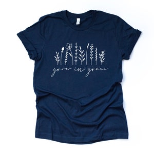 May include: Navy blue t-shirt with a white graphic of stylized flowers and the text "grow in grace".