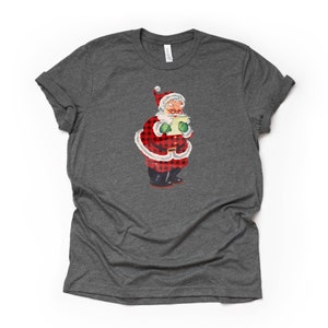 May include: A gray t-shirt with a vintage illustration of Santa Claus wearing a red and black plaid suit. Santa is holding a scroll and has a jolly expression on his face.