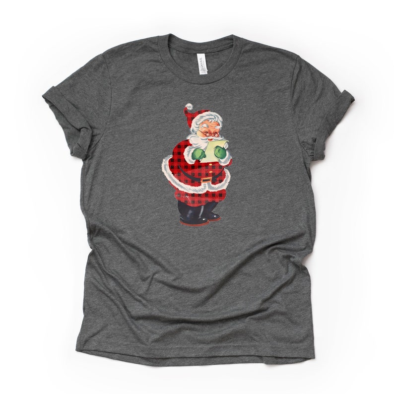 May include: A gray t-shirt with a vintage illustration of Santa Claus wearing a red and black plaid suit. Santa is holding a scroll and has a jolly expression on his face.