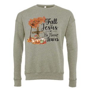 Puede incluir: Una sudadera verde con un dise&ntilde;o de oto&ntilde;o que presenta una cruz con estampado de leopardo, calabazas y hojas. El texto dice "Fall for Jesus He Never Leaves."
