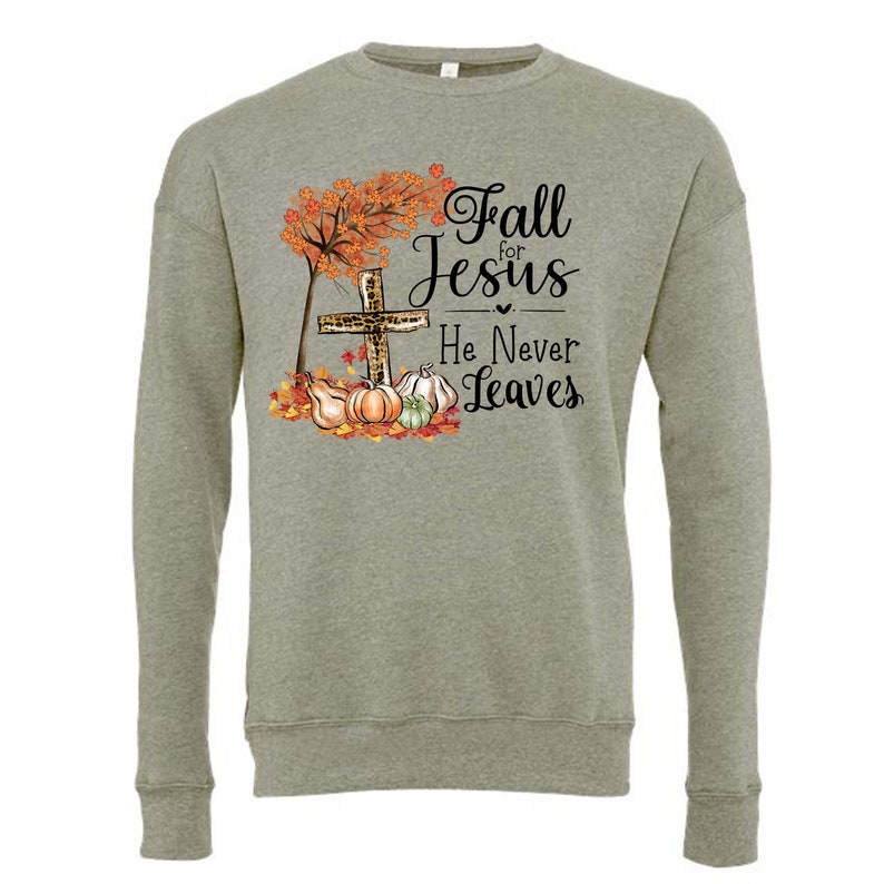 Puede incluir: Una sudadera verde con un dise&ntilde;o de oto&ntilde;o que presenta una cruz con estampado de leopardo, calabazas y hojas. El texto dice "Fall for Jesus He Never Leaves."