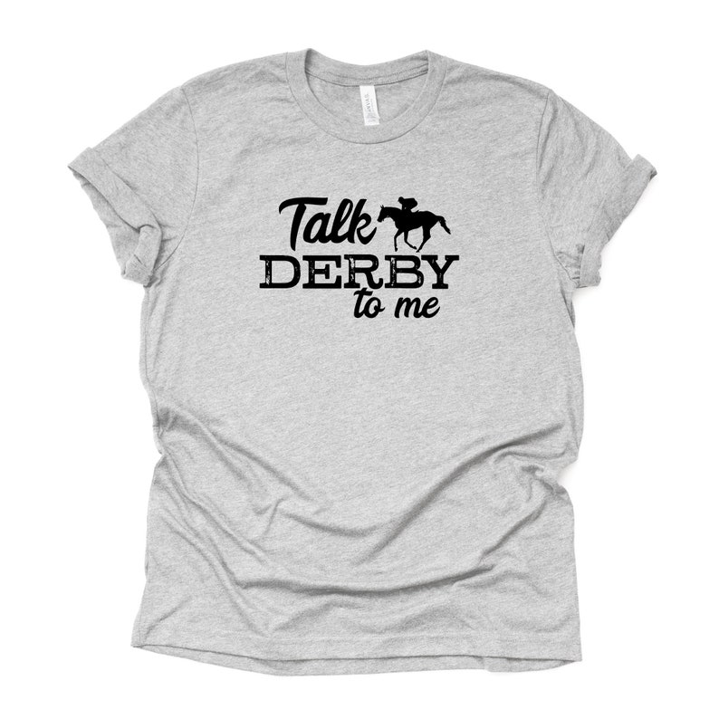 Peut inclure: Un t-shirt gris chin&eacute; avec un motif noir repr&eacute;sentant un cheval et un jockey avec le texte "Talk Derby to me".