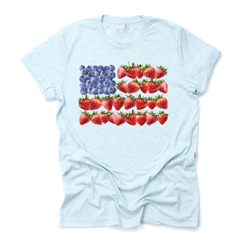 May include: Light blue t-shirt featuring a unique design of the American flag made from blueberries and strawberries. The flag design is centered on the front of the shirt. The shirt is made of a soft, lightweight material.