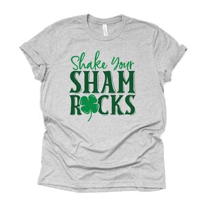 Puede incluir: Camiseta gris con el texto "Shake Your Shamrocks" en verde con un tr&eacute;bol verde.