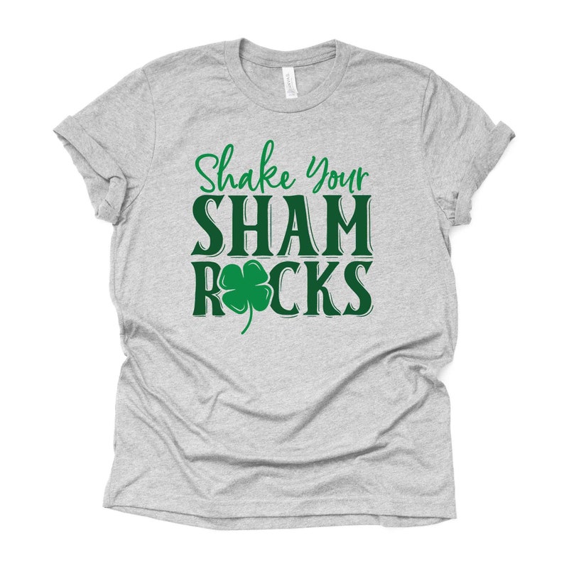 Puede incluir: Camiseta gris con el texto "Shake Your Shamrocks" en verde con un tr&eacute;bol verde.