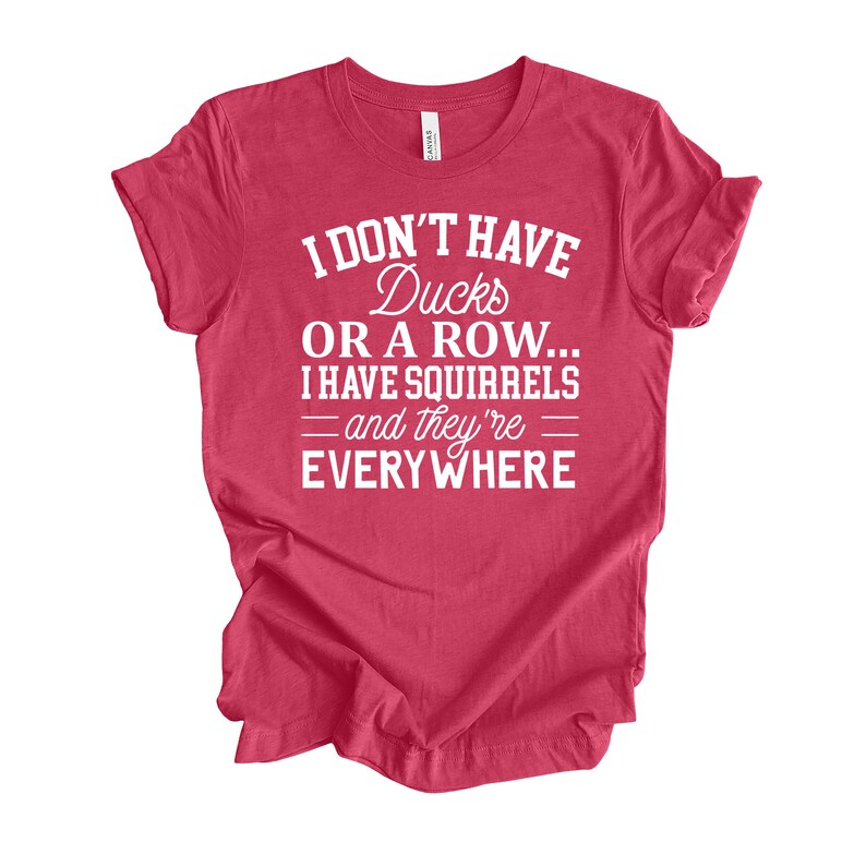 Peut inclure: T-shirt rouge avec du texte blanc qui dit "Je n'ai pas de canards ou une rang&eacute;e... J'ai des &eacute;cureuils - et ils sont partout"