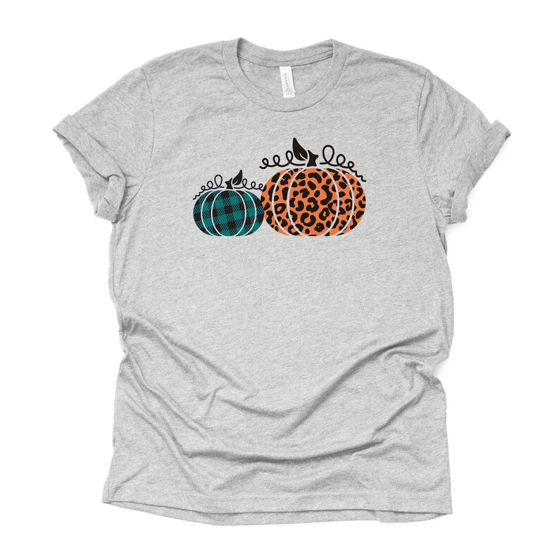 May include: A gray t-shirt with a design of two pumpkins. One pumpkin is teal plaid and the other is orange with a black leopard print.