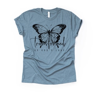 Peut inclure: Un t-shirt bleu clair avec un motif de papillon noir et le texte "transform&eacute; par l'amour de Dieu".