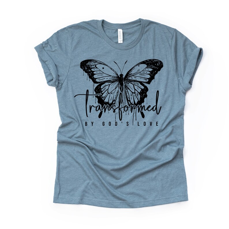 Peut inclure: Un t-shirt bleu clair avec un motif de papillon noir et le texte "transform&eacute; par l'amour de Dieu".