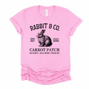 May include: Pink t-shirt with a black and white illustration of a rabbit and the text "RABBIT & CO.", "OPEN DAILY", "LOCALLY GROWN", "CARROT PATCH", "EGG HUNTS - JELLY BEANS - CHOCOLATE".
