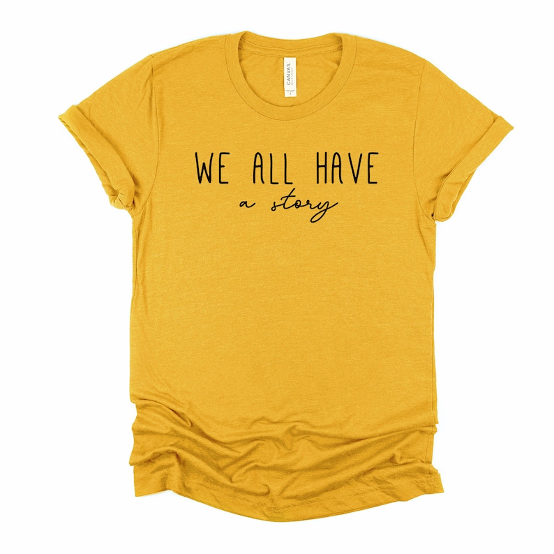 May include: A mustard yellow t-shirt with the text "WE ALL HAVE a story" printed in black.