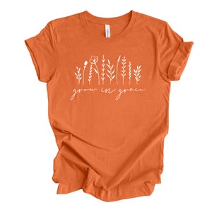May include: Orange t-shirt with a white graphic of stylized flowers and the text "grow in grace".