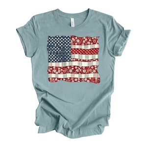 May include: A light blue t-shirt with a patchwork American flag design. The flag is made of different fabrics, including floral and plaid patterns.