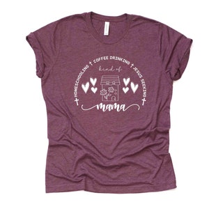 Puede incluir: Una camiseta color granate con un dise&ntilde;o gr&aacute;fico blanco que dice "Homeschooling + Coffee Drinking + Jesus Seeking + kind of mama". El gr&aacute;fico tambi&eacute;n incluye una casa con una flor y corazones.