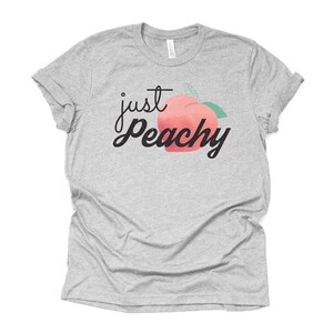 Może przedstawiać: Szary T-shirt z napisem "just peachy" czarnymi literami i grafiką brzoskwini.