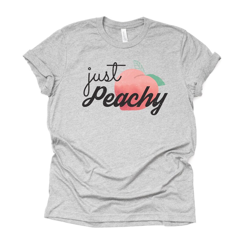 Może przedstawiać: Szary T-shirt z napisem "just peachy" czarnymi literami i grafiką brzoskwini.