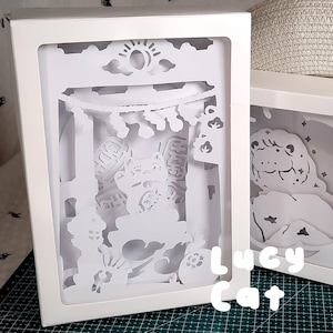 May include: White papercraft light box with a detailed cut-out design of a cat in front of a Japanese-style gate. The text "Lucy Cat" is visible below the box.