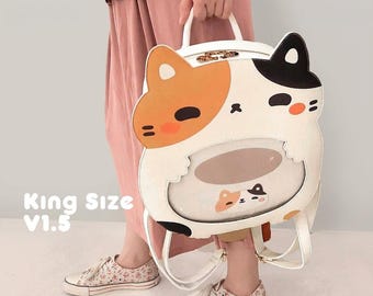 May include: A white backpack shaped like a calico cat with orange and black patches, featuring a clear window on the front, a top handle, and shoulder straps. The text "King Size V1.5" is printed in white on the lower left side of the image.