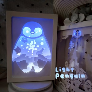 May include: A white light-up penguin papercraft with a blue glow. The penguin is surrounded by stars and a snowflake. The text "Light Penguin" is visible in the bottom right corner of the image.