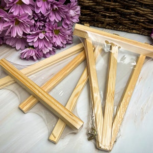 May include: Three wooden easel stands in a clear plastic bag. The easels are made of natural wood and are designed to hold small paintings or photos.